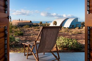 A wooden chair and a view of a modern house with a curved roof, situated in a dry landscape with sparse vegetation. - Casas Bioclimáticas Iter Casa Bernouilli (Granadilla de Abona)