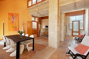 Ein geräumiges Zimmer mit Esstisch, weißen Stühlen, einer Blumenvase und einem Bild an der Wand.