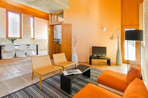 A modern living room with a sofa, chairs, a coffee table, a TV, and a dining area with chairs and a table. - Casas Bioclimáticas Iter El Caminito (Granadilla de Abona)