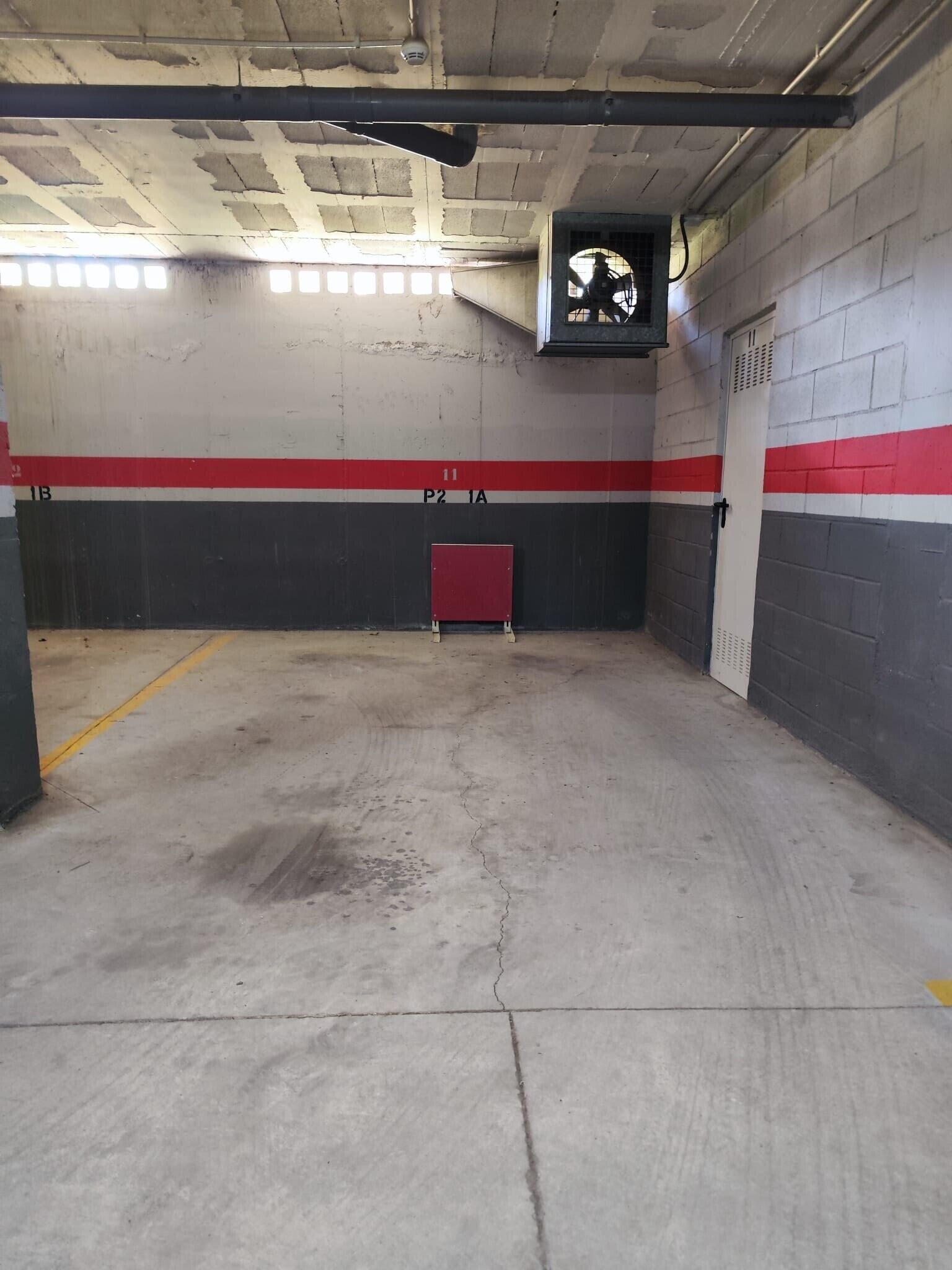 Un garaje para estacionar con pisos de concreto, paredes rojas y blancas, y un sistema de ventilación.