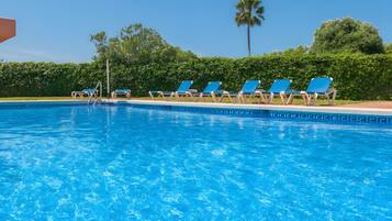 A swimming pool with clear blue water, surrounded by lounge chairs and a hedge.