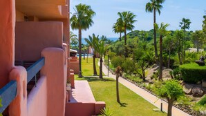Un balcón con vistas a un jardín ajardinado con palmeras y una piscina.