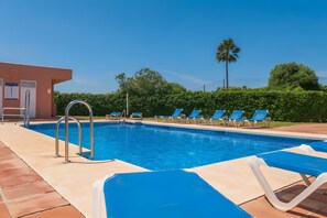 A swimming pool with blue water, surrounded by lounge chairs and a building with a door and windows.