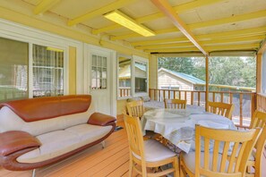 Ein überdachter Außenbereich mit Holztisch und Stühlen, einer Couch und Blick auf ein Haus im Hintergrund.
