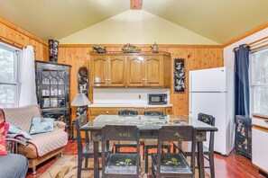 Ein gemütliches Blockhaus-Interieur mit Holzwänden, einem Esstisch mit Stühlen, einer Couch, einem Schrank mit Glastüren und einem Kühlschrank.
