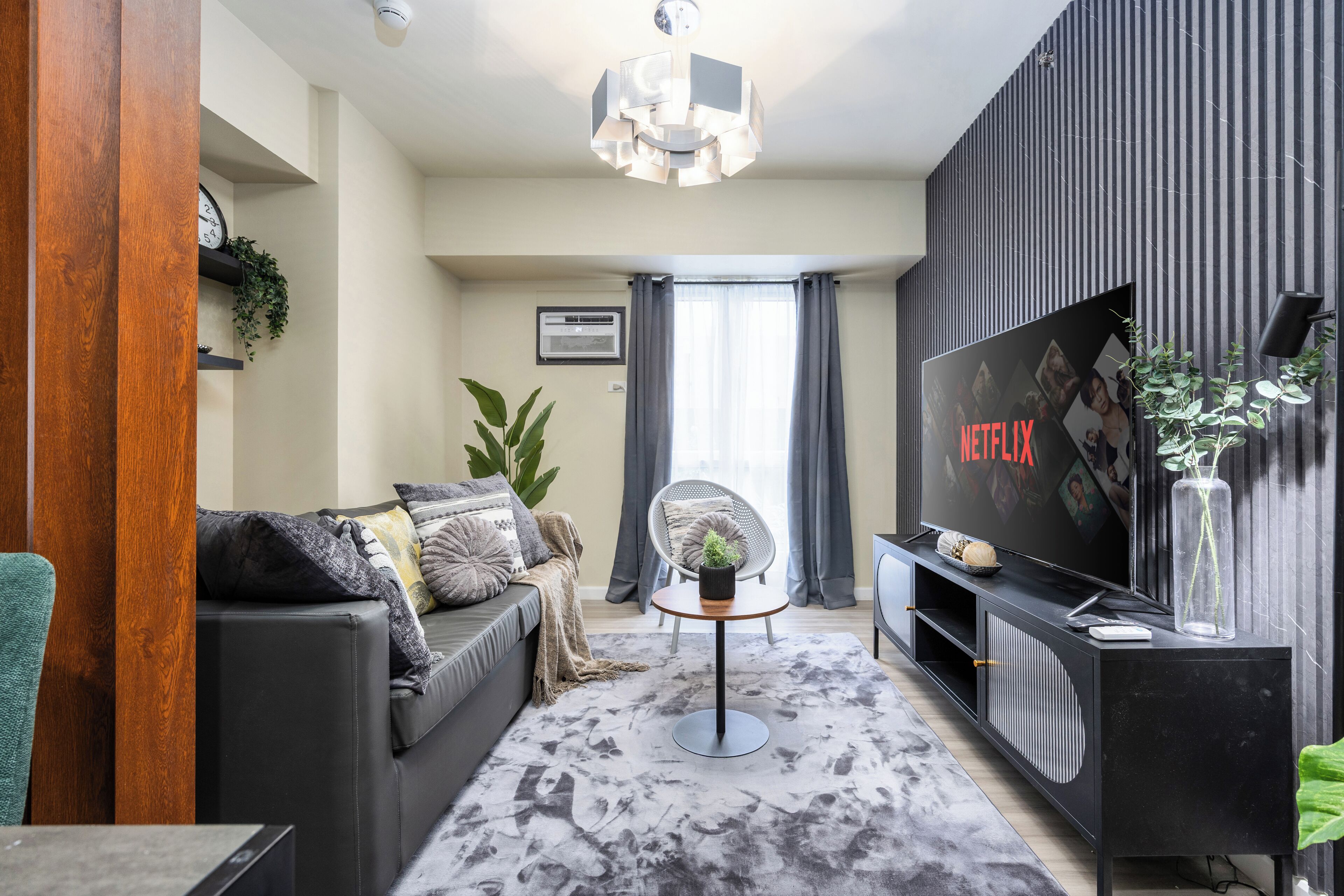 A modern living room with a grey sofa, a coffee table, a TV, and a large window with curtains.