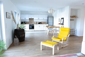 A modern kitchen with white cabinets, a dining area with wooden chairs, and a bright yellow armchair. - Apartment 'Ferienwohnung Zweitblick Koblenz' with Balcony and Wi-Fi (Koblenz)