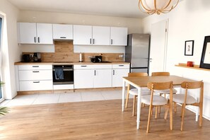 Eine moderne Küche mit weißen Schränken, einem Edelstahlkühlschrank und einem Holztisch mit Stühlen.