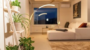 En moderne stue med en hvid sofa, en træstige med planter, en gulvlampe og et stort vindue.