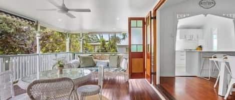 A covered outdoor dining area with wicker furniture, a ceiling fan, and a view of a white kitchen.