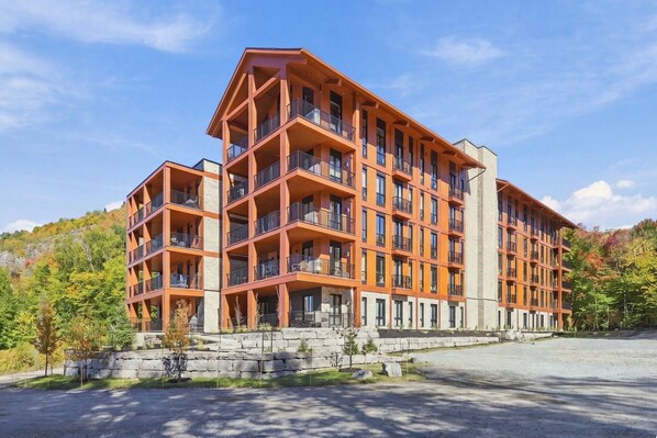 Un hôtel à plusieurs étages, doté de balcons, d’une façade en pierre et d’un espace de stationnement.