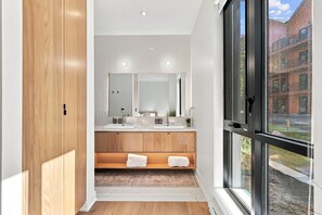 A modern bathroom with a large mirror, wooden vanity, and a view of a building through a large window. - Modern Mont-Tremblant Getaway -Ostrya (Mont-Tremblant)