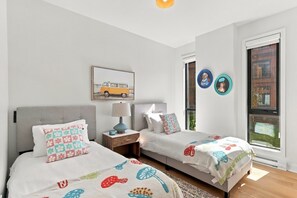 Une chambre avec deux lits, une table de chevet, une lampe et une fenêtre avec des stores.