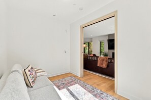 Ein modernes Wohnzimmer mit einer Couch, einem gemusterten Teppich und einer Schiebetür, die zu einem Essbereich mit Fernseher führt.