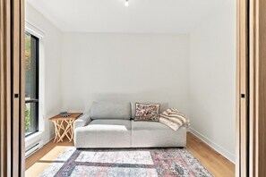 Un salon moderne avec un canapé gris, un tapis à motifs et une petite table d’appoint en bois sur laquelle est posé un jeu d’échecs.