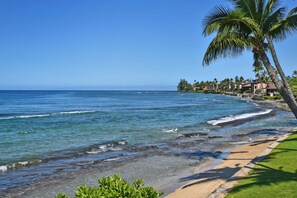 A beach with clear blue water, a sandy shore, and a row of buildings in the background. - Garden View Condo Just Steps from the Ocean -Maui Sands Seaside 717 (Lahaina)