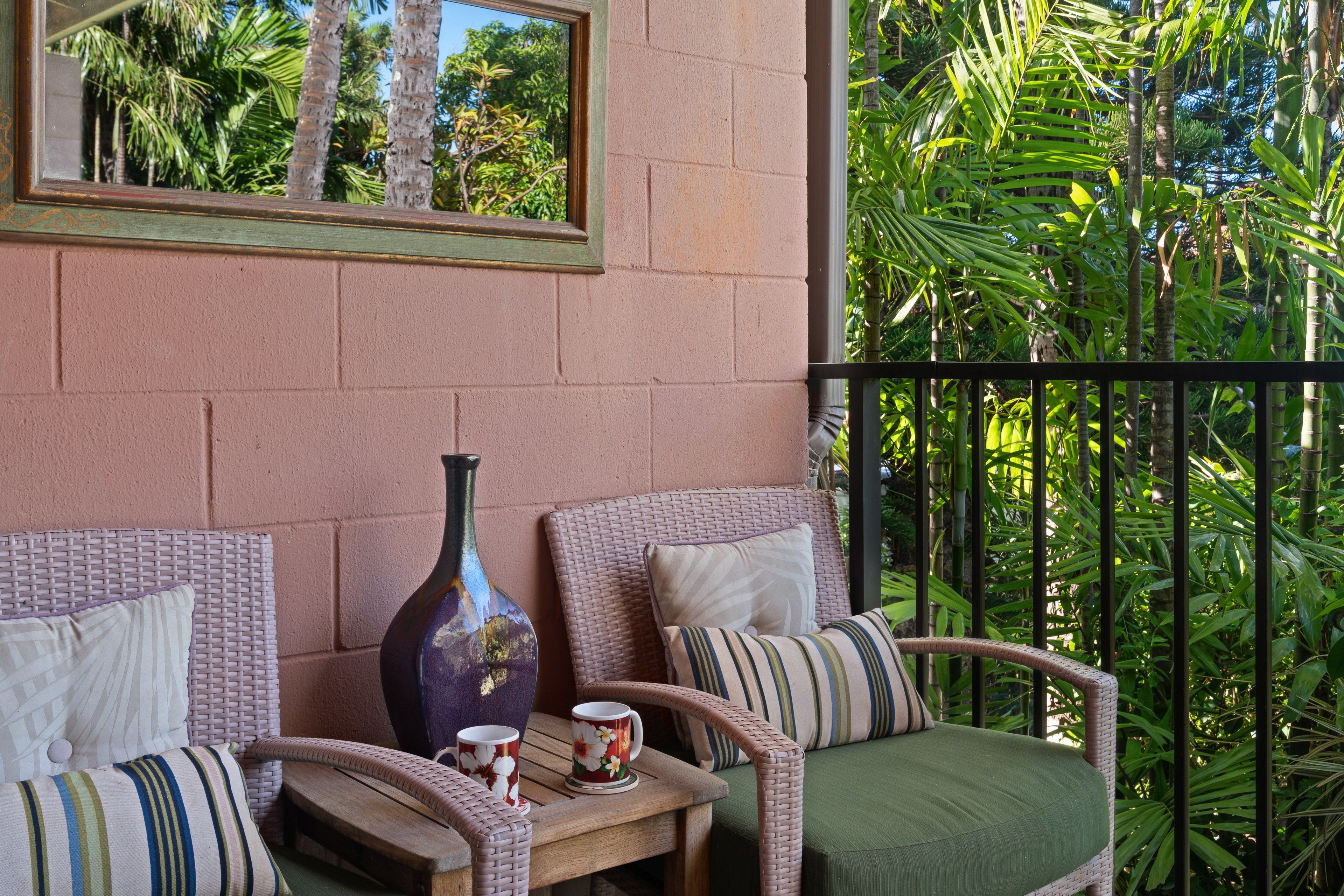 A balcony with wicker furniture, a vase, and a table with two mugs.