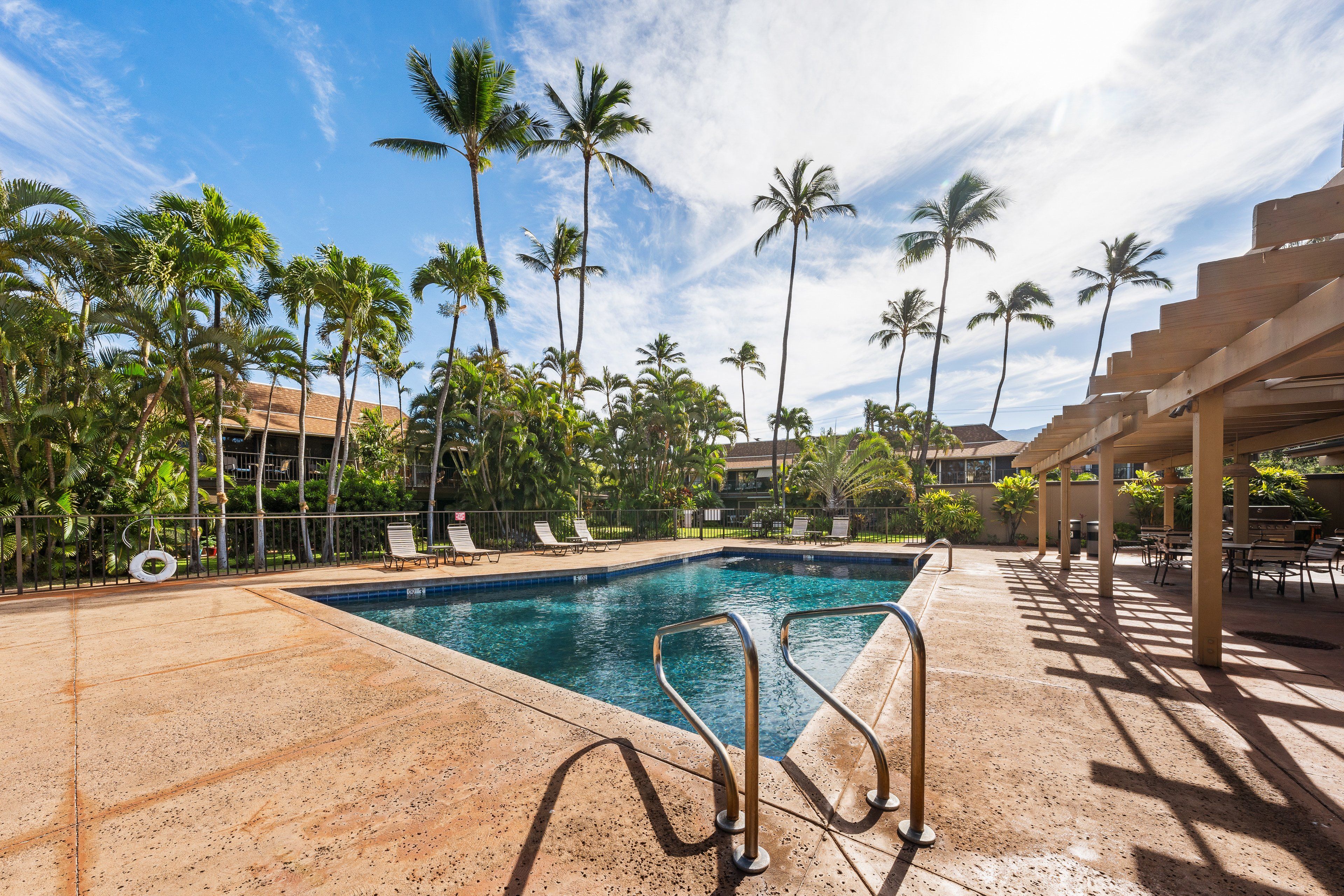 A pool area with clear blue water, surrounded by palm trees and lounge chairs.