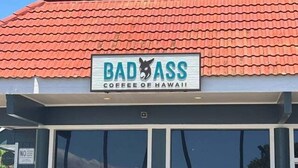 Una fachada con un letrero que dice 'BAD ASS COFFEE OF HAWAII' y un tejado de tejas rojas.