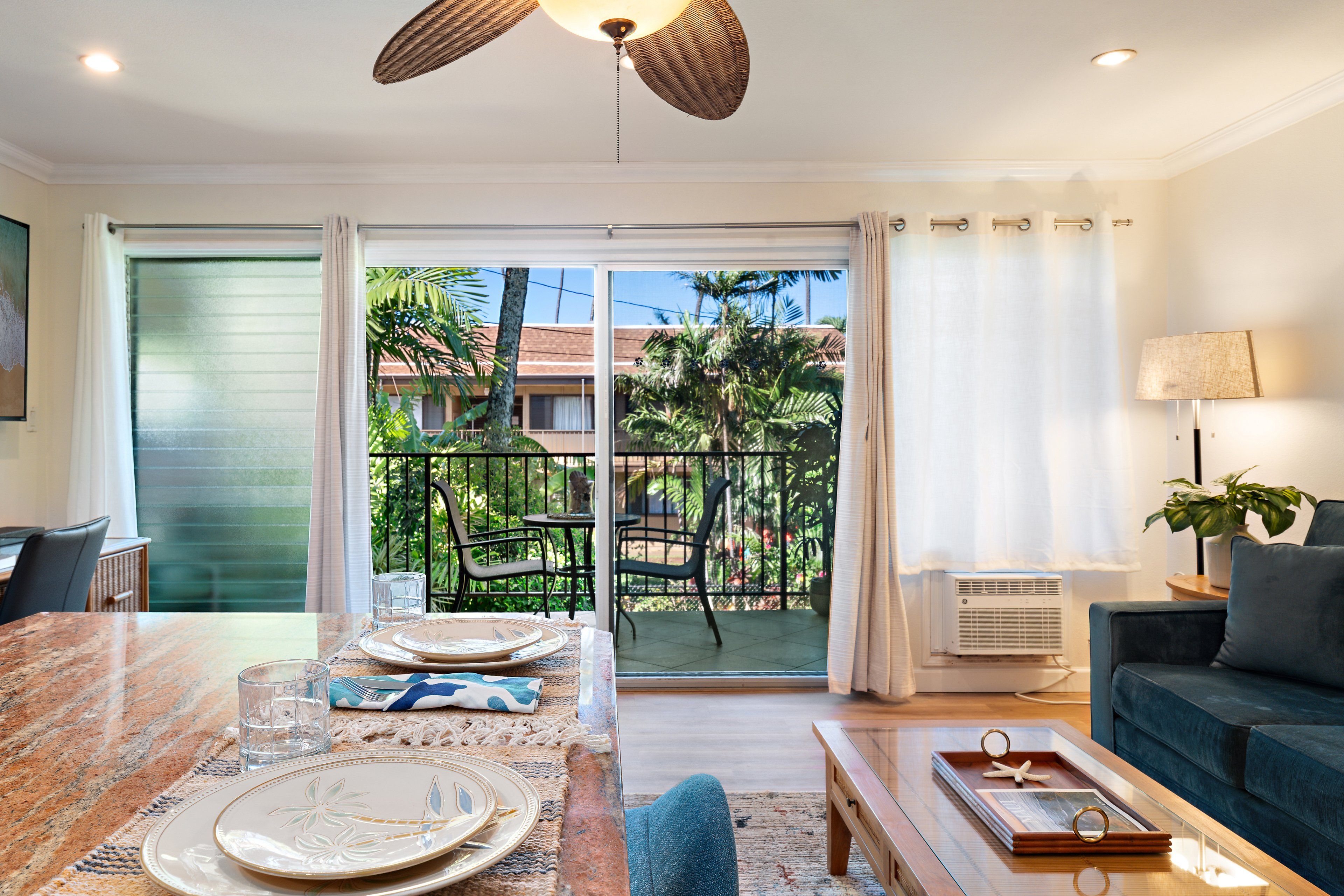 A dining area with a table set for two, a sofa, and a balcony with outdoor furniture.
