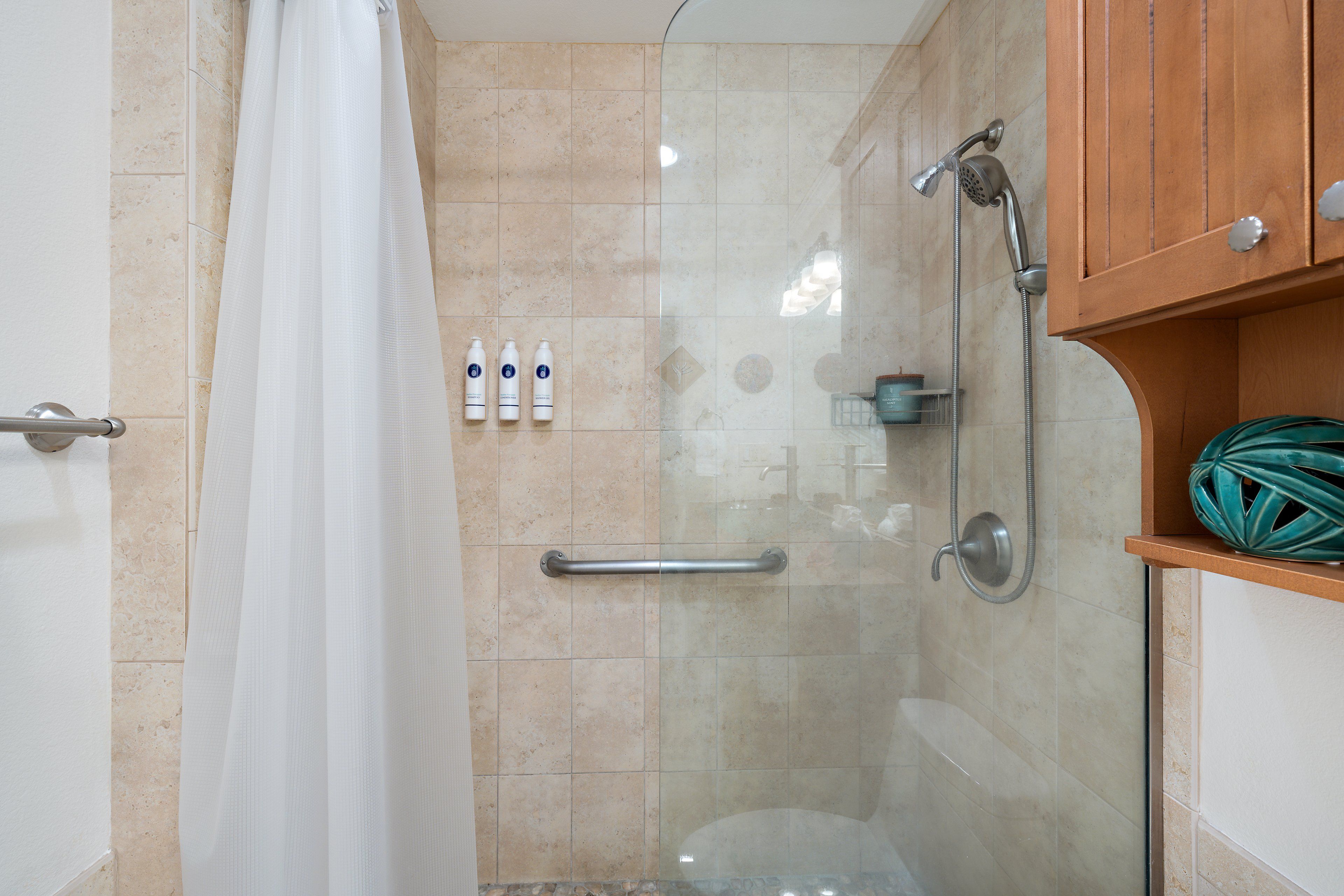 A bathroom with a glass shower enclosure, a white shower curtain, and a wooden cabinet with a green decorative item.