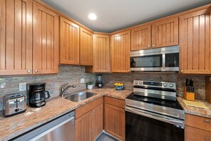 A kitchen with wooden cabinets, a stainless steel microwave, an oven, a coffee maker, and a sink. - Garden View Condo Just Steps from the Ocean -Maui Sands Seaside 717 (Lahaina)
