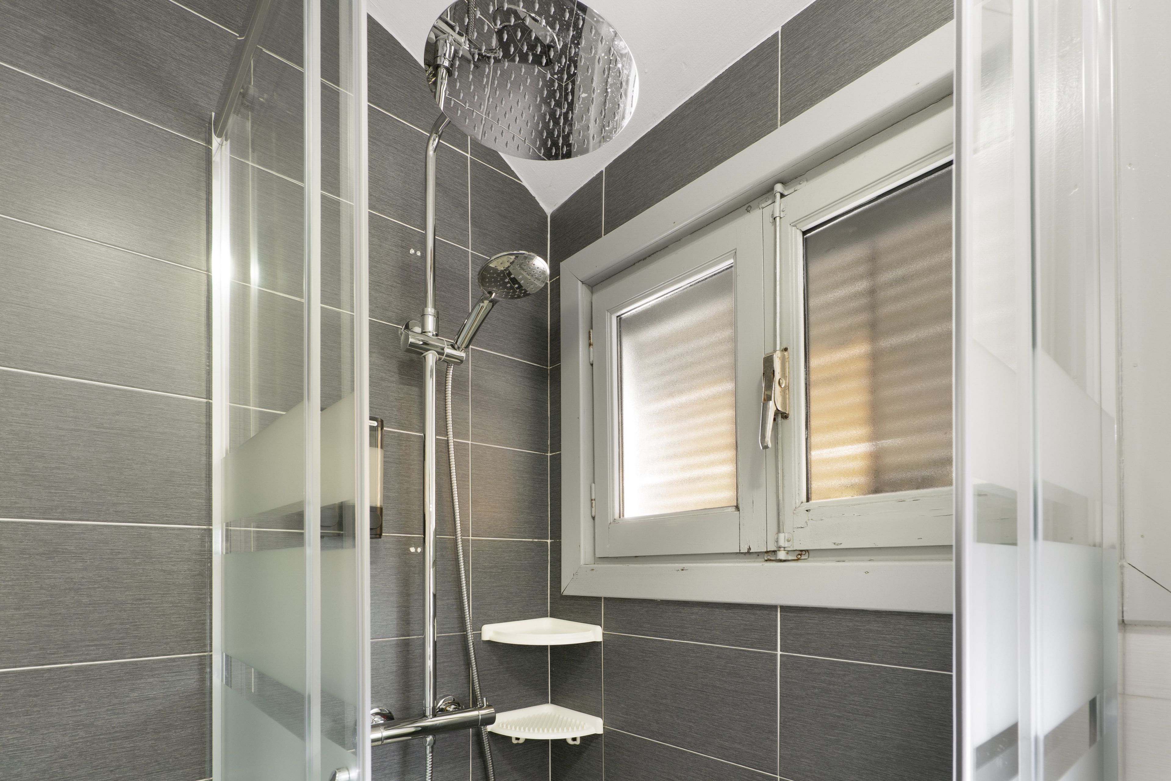 Un box de ducha moderno con puerta de cristal, ducha de mano y rociador manual.