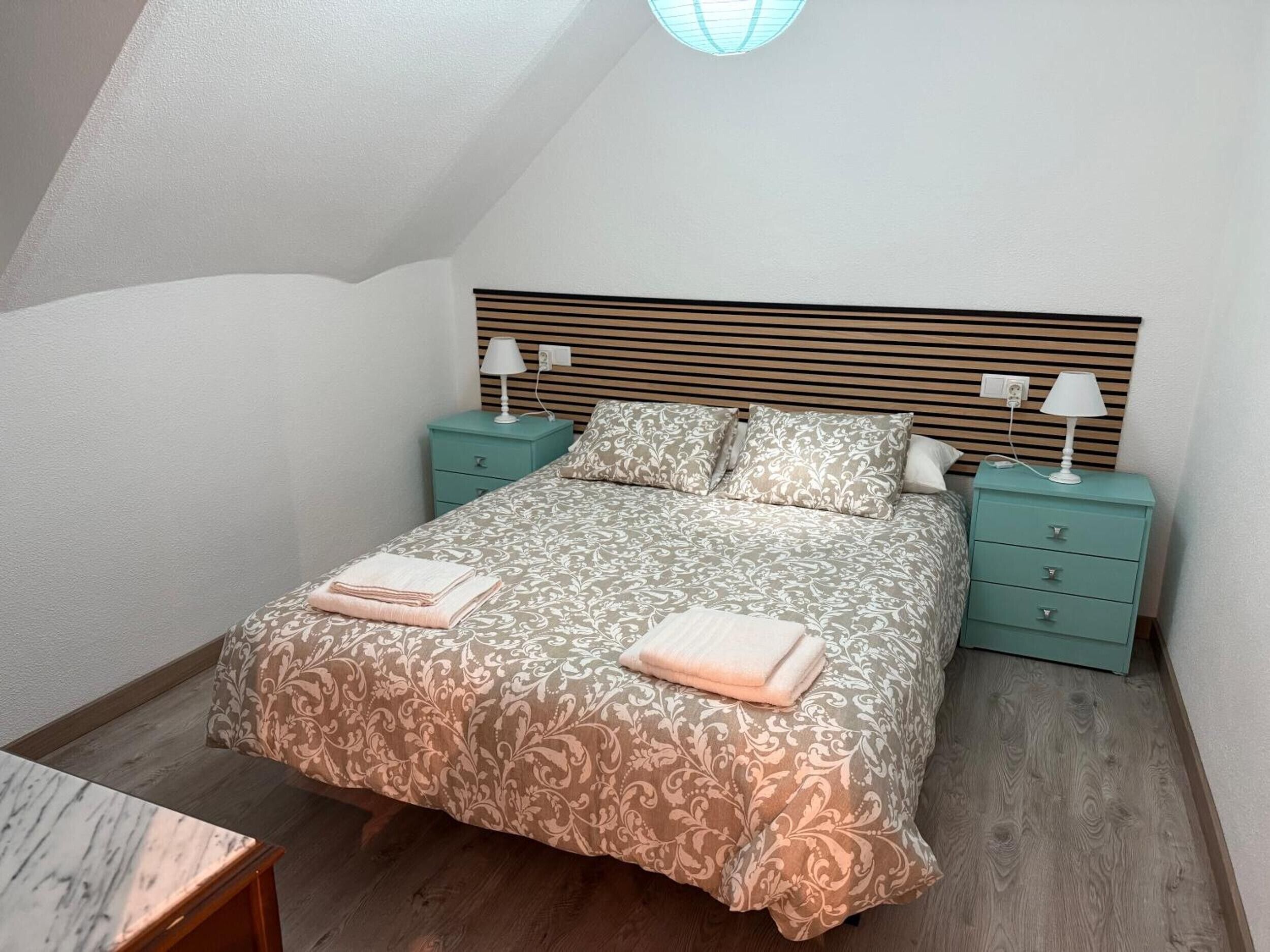 Un dormitorio con una cama, dos mesitas de noche, una lámpara en cada una y un cabecero de madera.