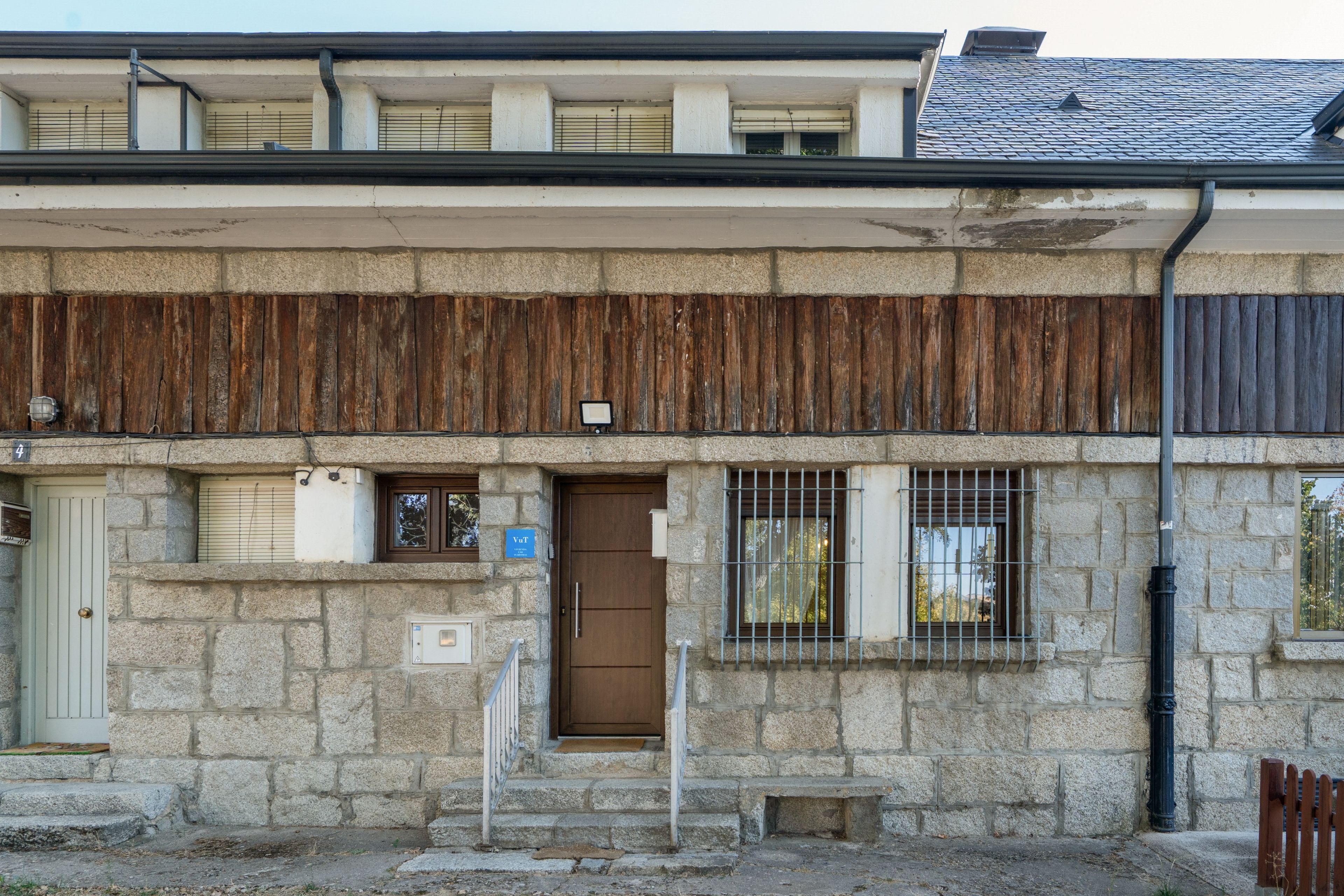 A stone building with a wooden facade, a metal gate, and a small window with a metal grill.