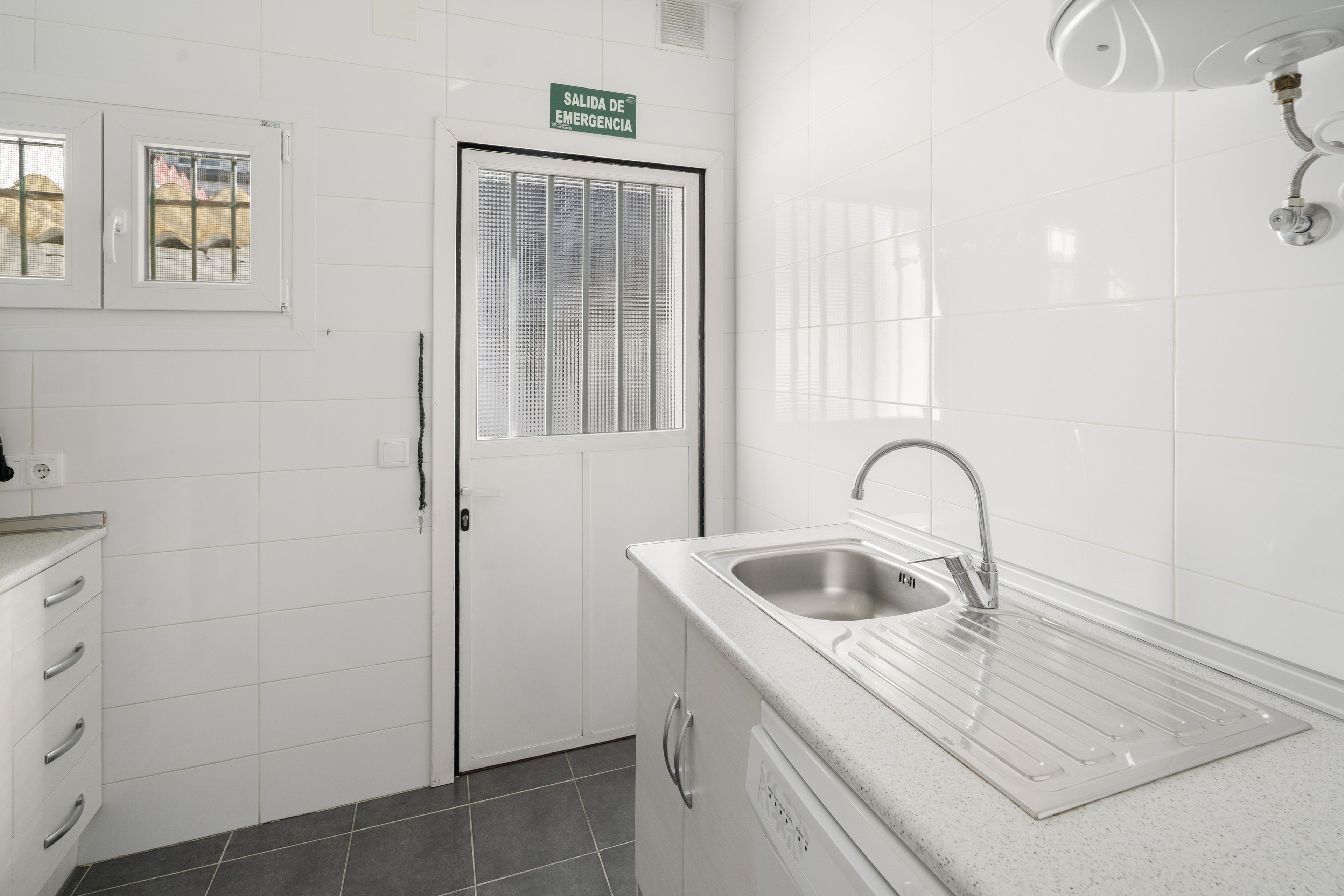 Een schone, moderne badkamer met een wastafel, spiegel en een deur met de tekst 'SALIDA DE EMERGENCIA', wat een nooduitgang aangeeft.