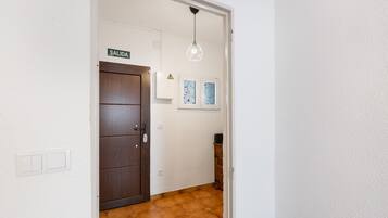 Un pasillo con una puerta marrón, una pared blanca, piso de baldosas, una lámpara en el techo y un pequeño armario.