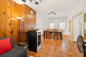 A room with a fireplace, a dining table with chairs, a sofa, and a fan.