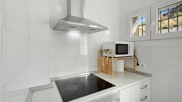 Una cocina moderna con azulejos blancos, una campana extractora de acero inoxidable, un microondas sobre un soporte de madera y una placa de inducción integrada.