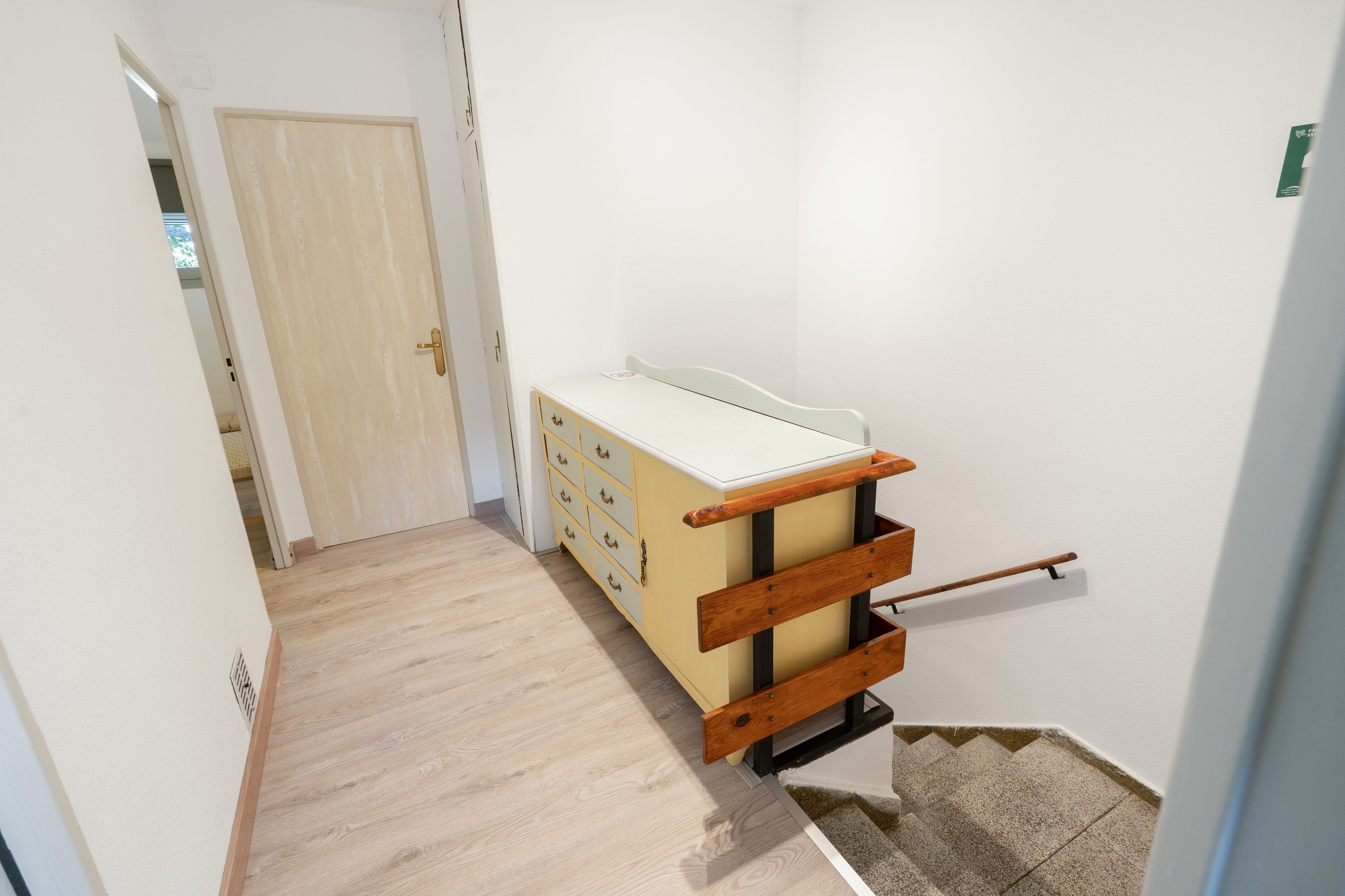 A hallway with a wooden bench, a door, and a small table with drawers.