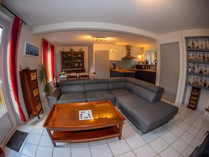 Una sala moderna con un sofá modular, una mesa de centro de madera y un comedor con un armario y una mesa.