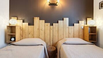 A room with two beds, a wooden headboard, bedside tables with lamps, and a wall-mounted light fixture.