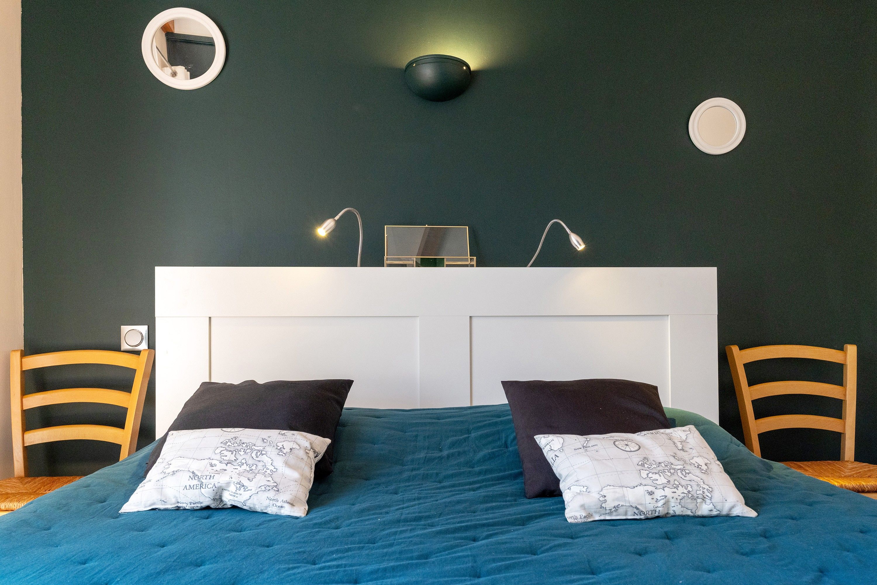 Une chambre à coucher comprenant un lit, deux chaises, un bureau et une lampe fixée au mur.