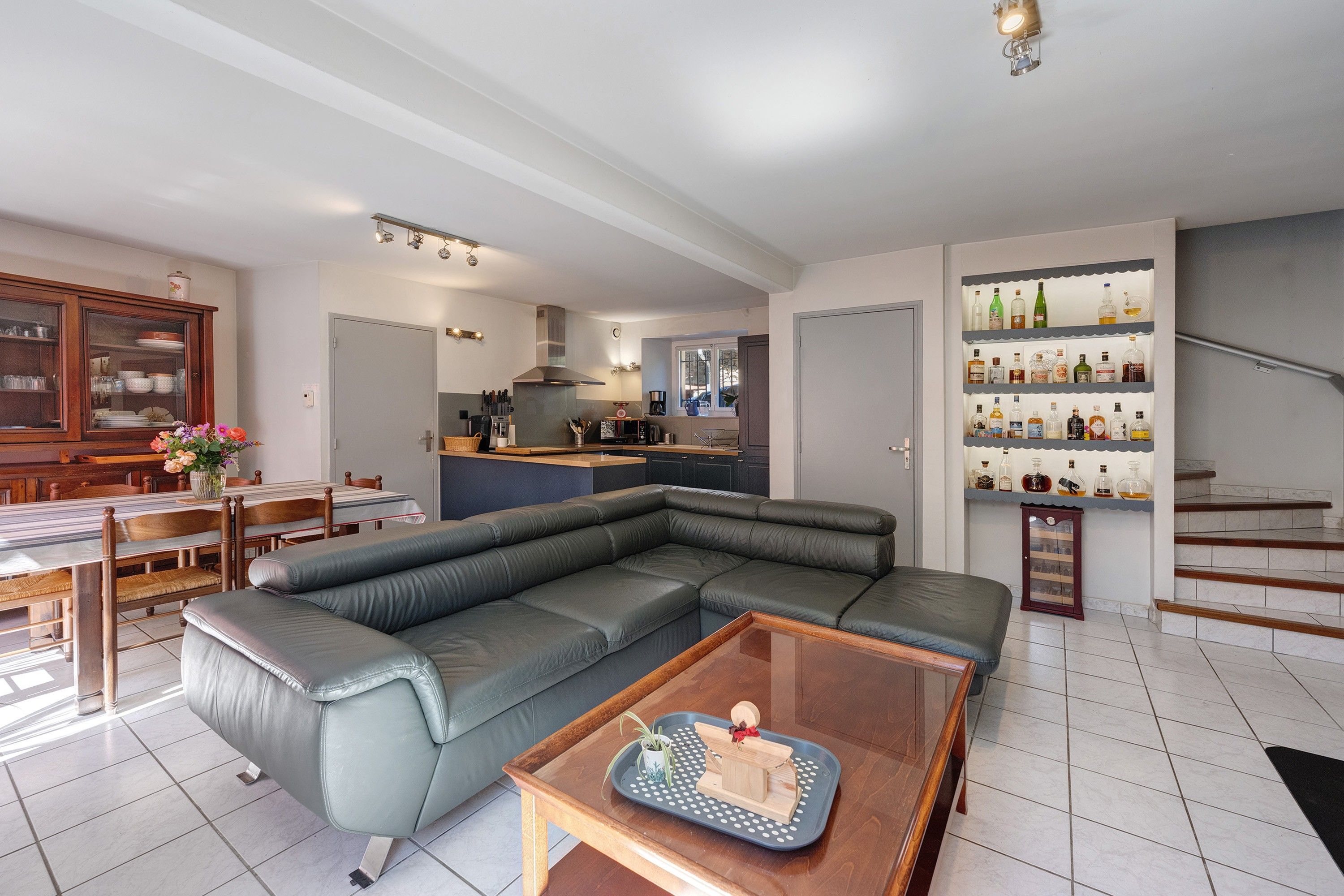 Una sala moderna con un sofá seccional, una mesa de comedor con sillas, una zona de cocina y una escalera con un aparador.