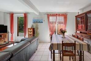 Habitació amb sofà, taula de dinar, cadires, televisió i finestra amb cortines.