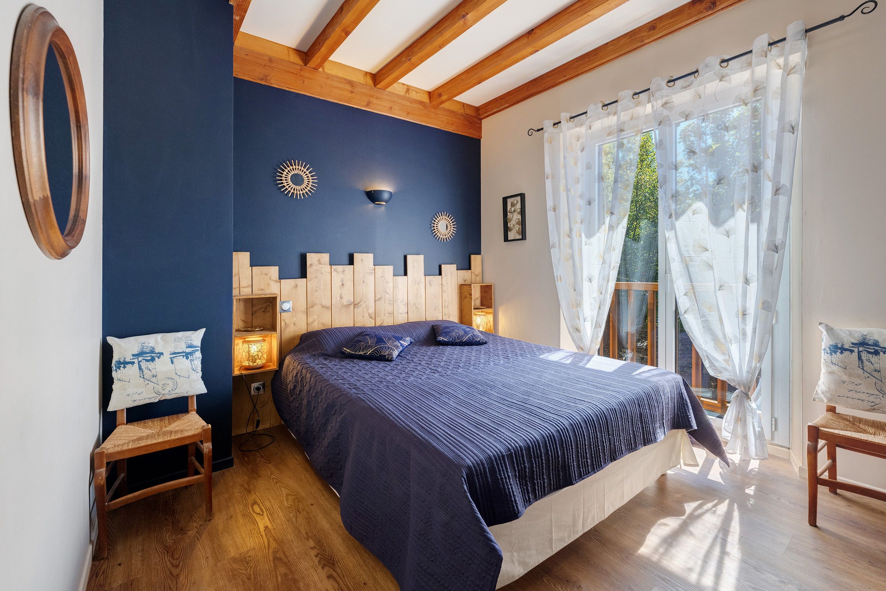 Een slaapkamer met een groot bed, een houten hoofdbord, twee wandlampen, een nachtkastje, een klein tafeltje en een stoel.