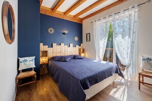 Un dormitorio con una cama grande, cabecera de madera, dos lámparas de pared, una mesita de noche, una pequeña mesa y una silla.