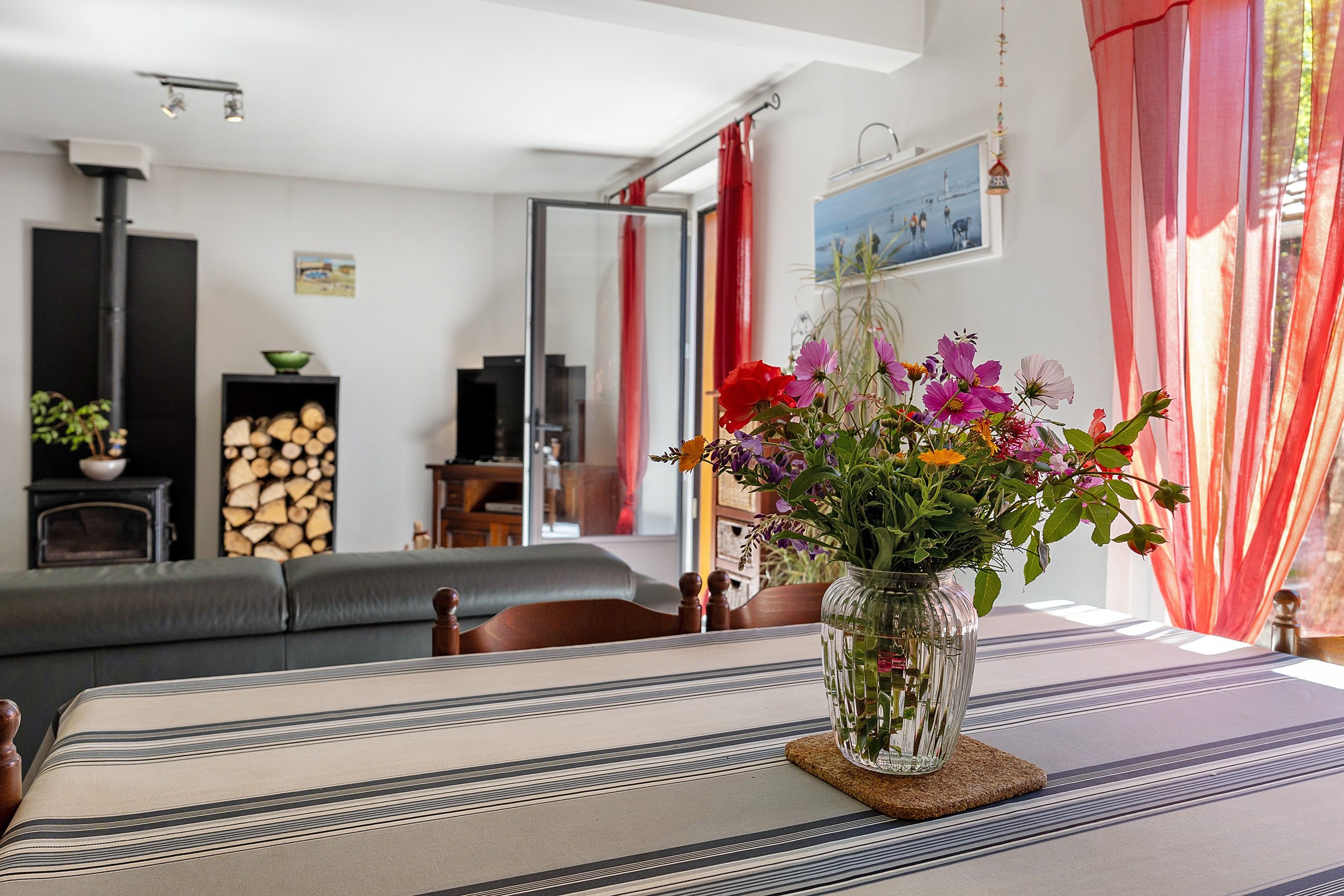 Een woonkamer met een bank, een tafel met een bloevas, een open haard en een raam met gordijnen.