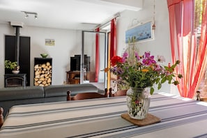 En stue med sofa, bord med blomster, pejs og vindue med gardiner.