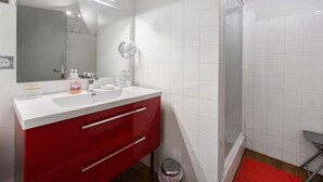 A modern bathroom with a white sink, red cabinet, and a glass shower enclosure.