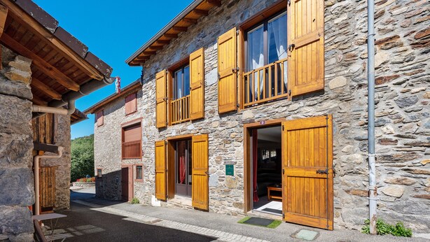 A stone building with wooden shutters and a balcony, featuring a clear sky.