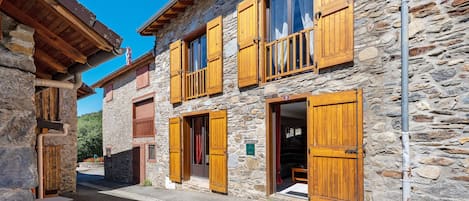 Un bâtiment en pierre avec des volets en bois et un balcon, sur fond de ciel dégagé.