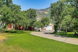 Ein Auffahrt, die zu einem Haus mit Garage führt, umgeben von üppigen, grünen Bäumen und einer hügeligen Landschaft im Hintergrund.