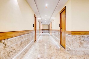 A hotel corridor with marble flooring, wooden door frames, and recessed ceiling lighting.