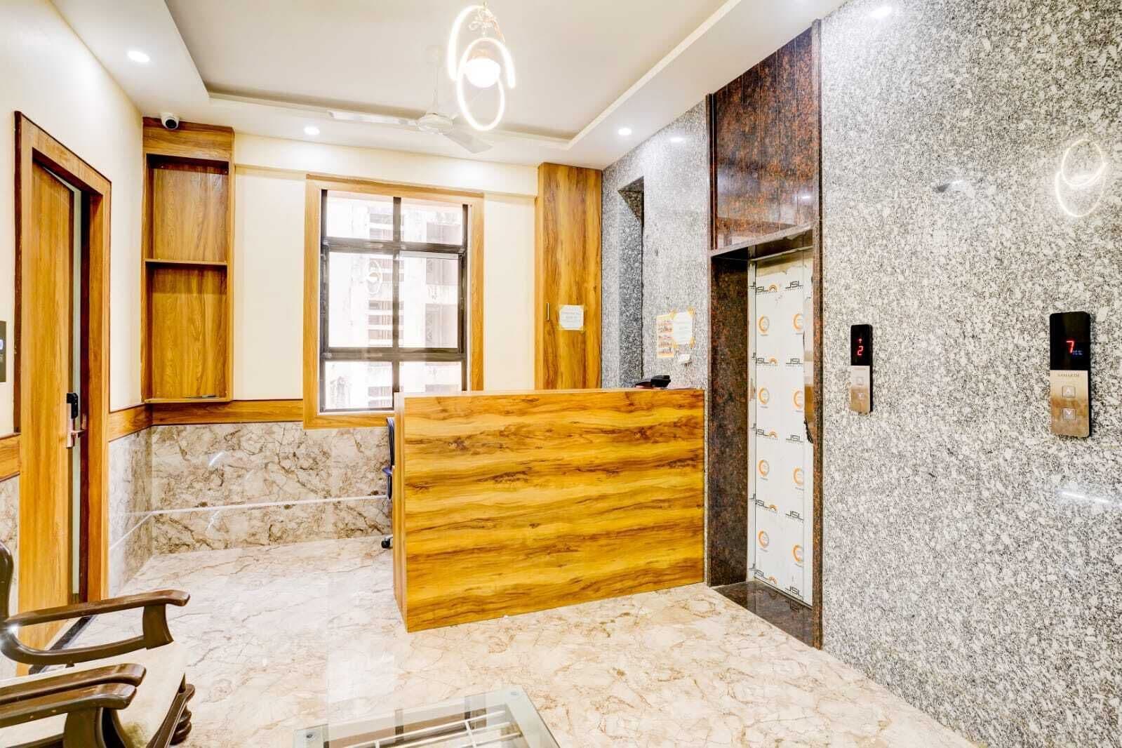 A hotel reception area with a marble floor, wooden reception desk, and a modern elevator.