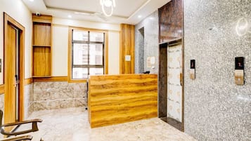 A hotel reception area with a marble floor, wooden reception desk, and a modern elevator.